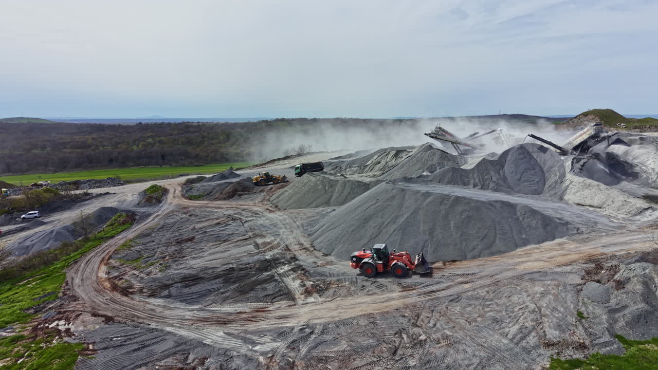 Granite quarry is active with heavy machinery moving materials and workers operating equipment in a rural area during daylight