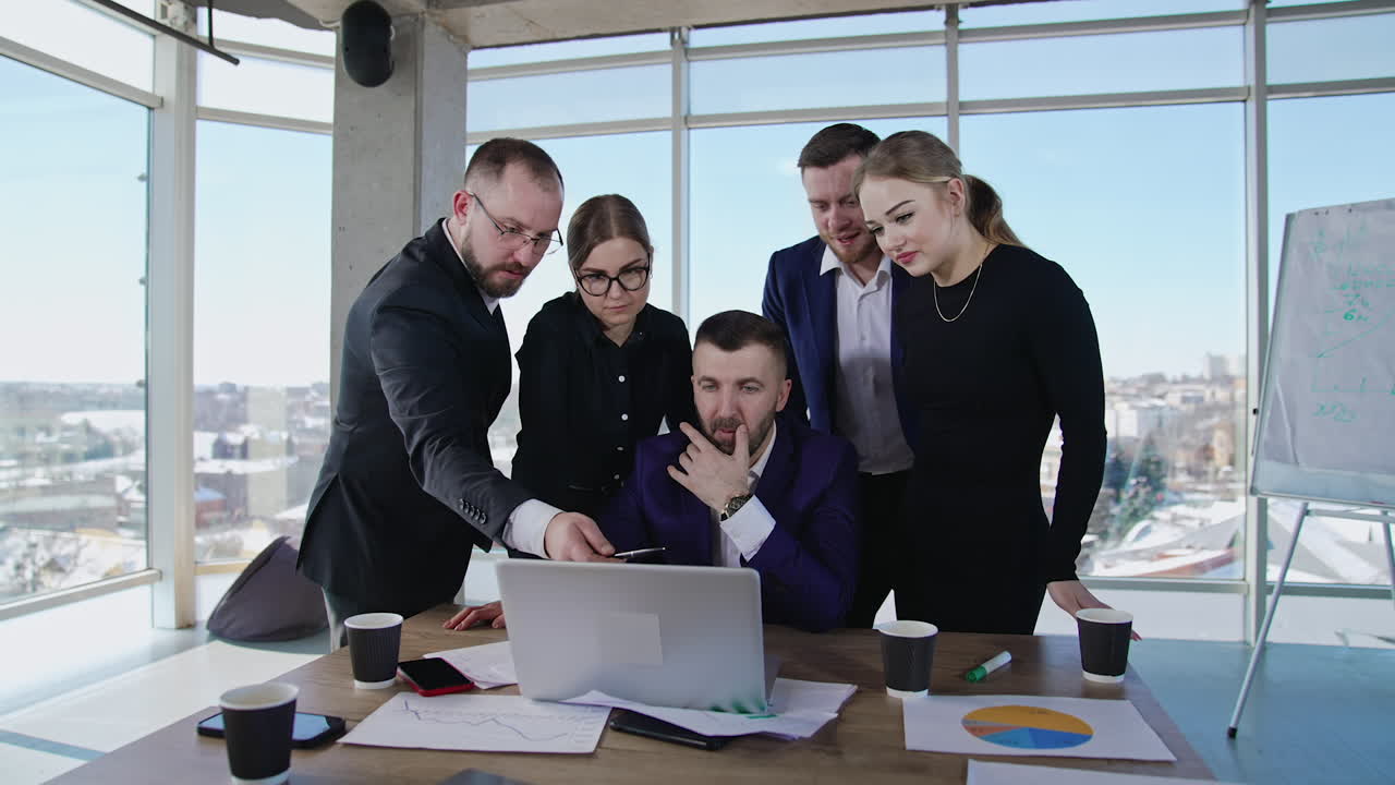 Teammates stand around the table and laptop. Team of males and females discuss something on computer screen. Friendly communication of coworkers in the office.