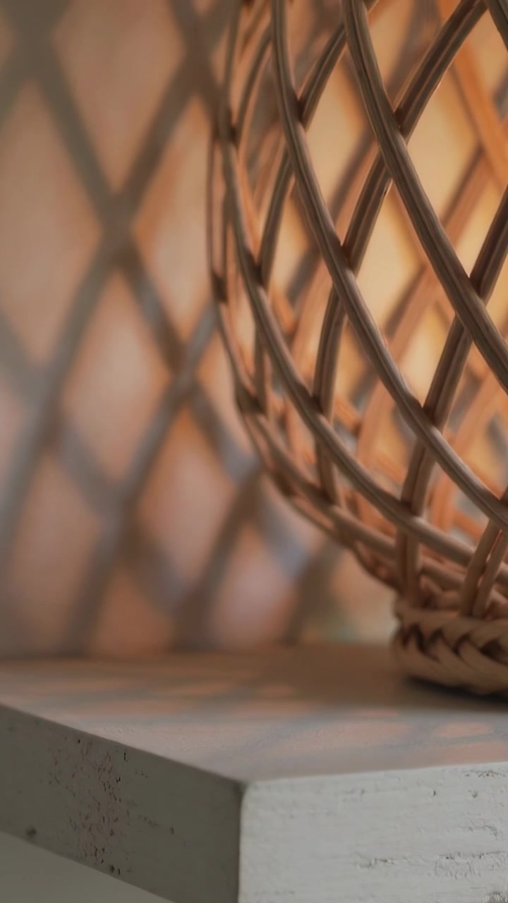 Video verticale: Telecamera che si sposta rivelando una lampada in rattan accesa su uno scaffale dipinto, mostrando un'ombra a griglia.