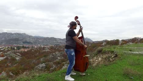 hombre tocando el contrabajo en una pintoresca cima de la montaña