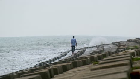 외로운 남자가 천천히 해변을  ⁇ 고 있습니다. 해변 침식 보호 엔지니어링 콘크리트로 보호되어 있습니다.
