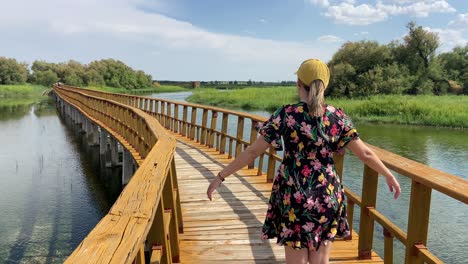 Mujer-Caucásica-Con-Vestido-De-Flores-Y-Gorra-Caminando-En-Tablas-Del-Parque-Nacional-Daimiel