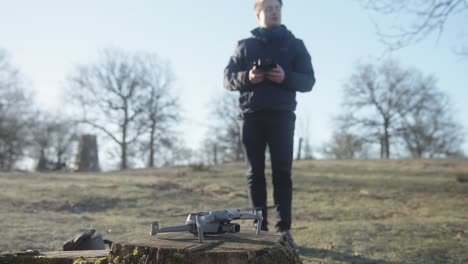 young male dronepilot setting up a drone and lift off into the air with remote control for flying on a drone operation in nature on a cold spring morning