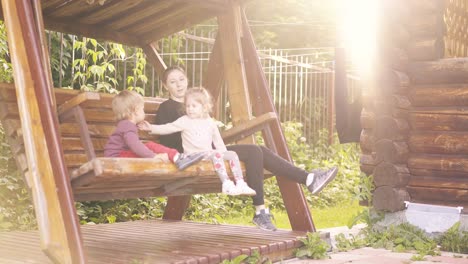 young pretty mother with children swinging on a wooden swing near the summer house on vacation