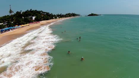 muñeca aérea volando sobre personas nadando en el mar turquesa cerca de la orilla de arena en la playa de mirissa durante el día, sri lanka