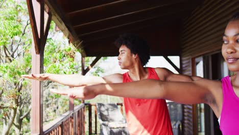 Happy-african-american-couple-doing-yoga-and-stretching-in-log-cabin,-slow-motion