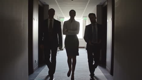 two businessmen and a businesswoman in elegant clothes walking down a corridor