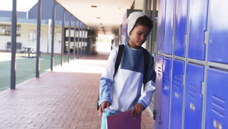 in a school hallway, a young african american student stands by blue lockers with copy space