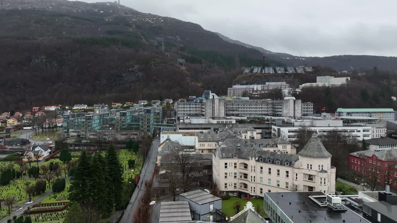 Haukeland Hospital with Ulriken Mountain in the background and a graveyard in the foreground. Slow aerial rise on an overcast day
