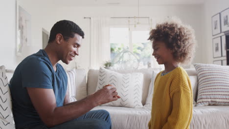 Pre-teen-African-American-girl-giving-her-dad-a-cup-and-saucer-she’s-made-from-clay,-over-side-view