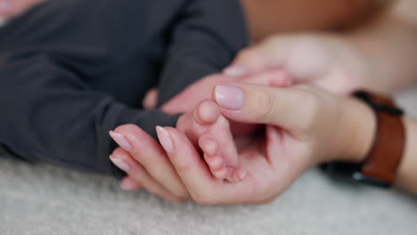 female hand with brown wrist watch strokes tiny baby toes. cute infant's feet in mother's hands. close up.