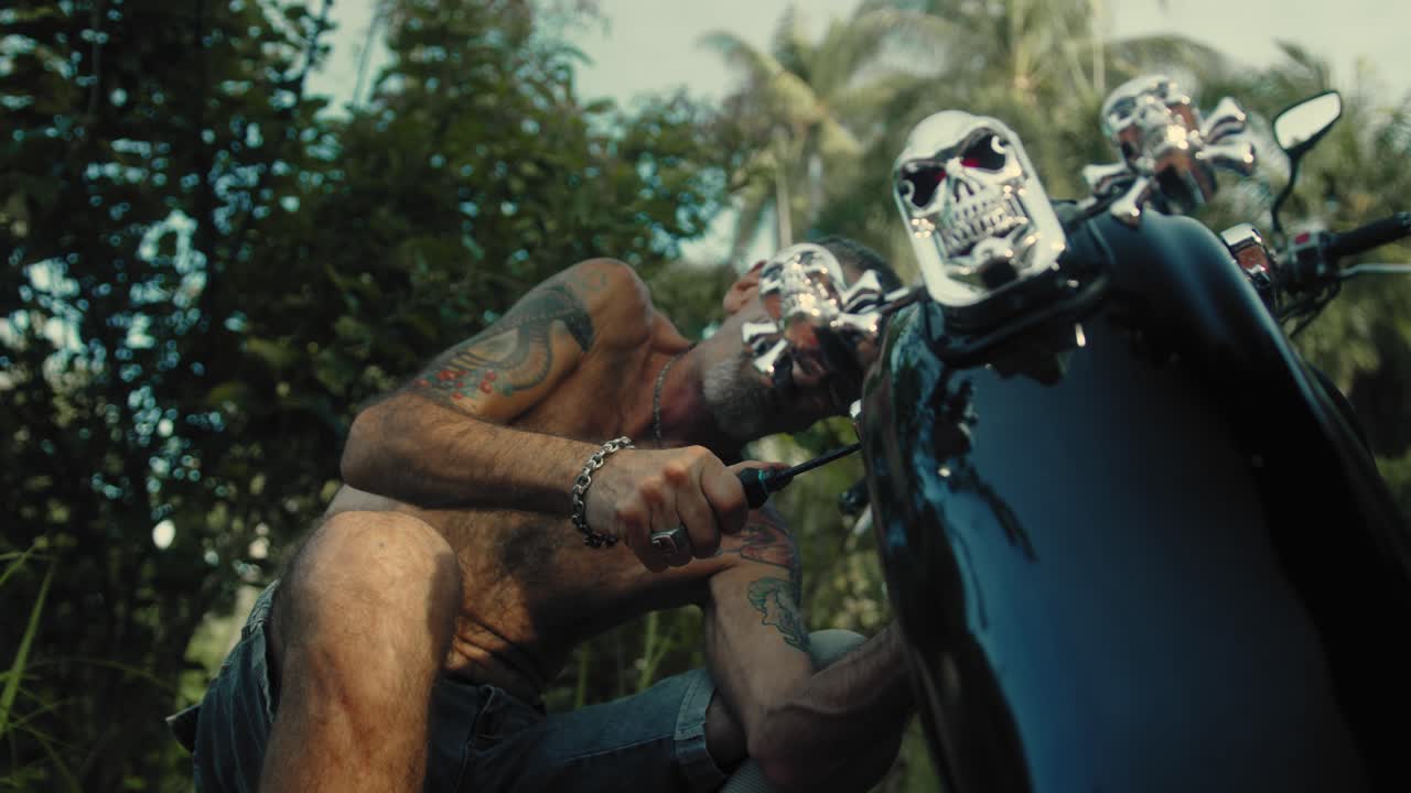 Man repairing his custom motorcycle in a tropical jungle environment