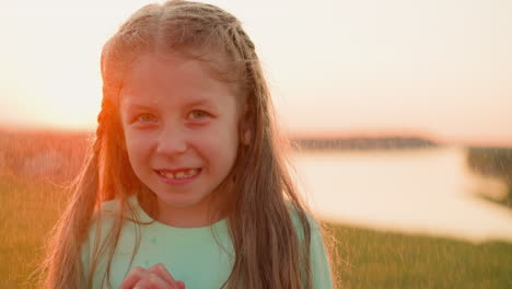 cute kid stands under raindrops at riverside positive little girl with long hair smiles with
