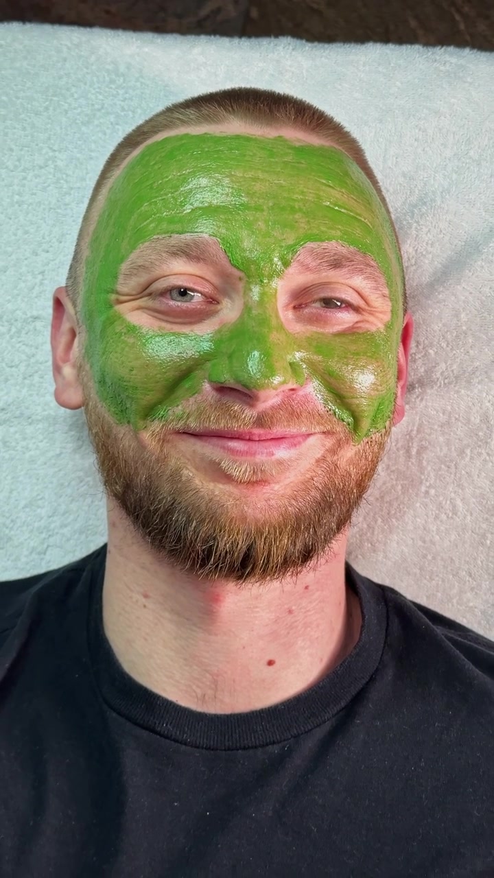 Homem aplica máscara facial verde durante tratamento facial em salão de beleza durante o dia