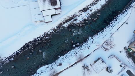 rocky river stream flowing through small swiss town in winter snow