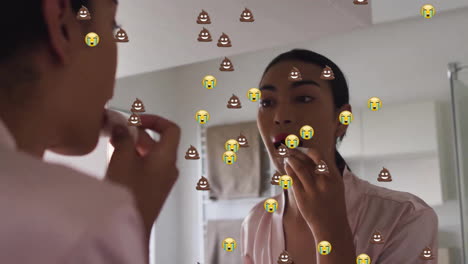 Animation-of-emoji-icons-over-biracial-woman-applying-lipstick