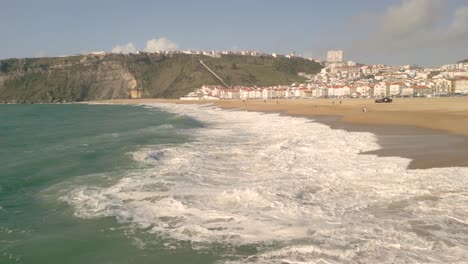 grandes olas que golpean la orilla durante la temporada de verano y suburbio en la distancia en nazare, portugal