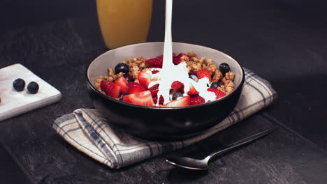 leche súper lenta se está vertiendo en un tazón con granola de cereales con fresas y arándanos en rodajas, desayuno saludable. filmado con cámara de alta velocidad a 420 fps