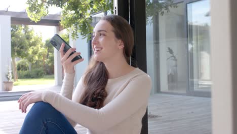 mujer caucásica feliz sentada en el suelo y hablando en el teléfono inteligente en cámara lenta