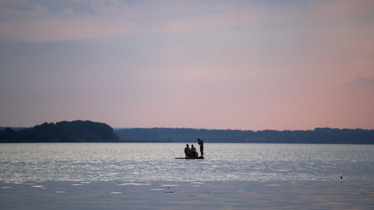 Young men floating in a catamaran on the river. Water background and two guys sitting in pedal boat while one man standing near in the evening.