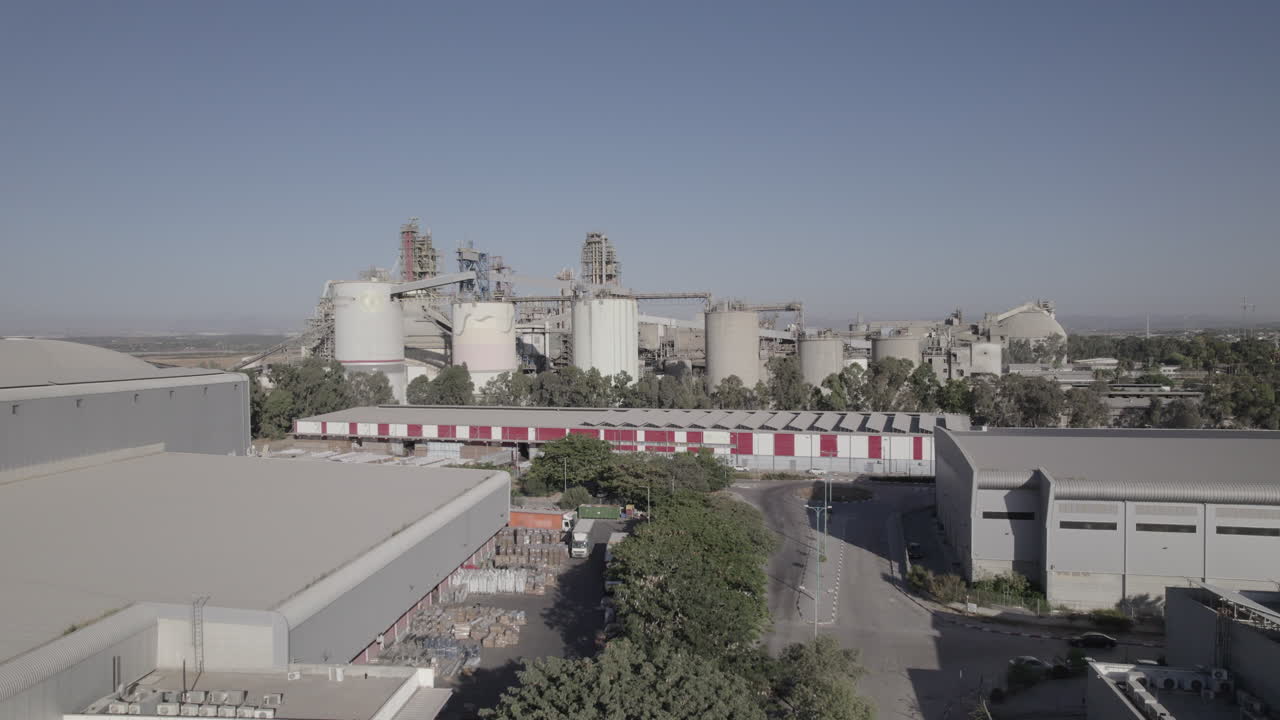 toma aérea de una enorme fábrica de cemento, una zona industrial innovadora con muchos hangares y camiones, una hermosa zona con árboles, toma de empuje