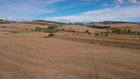 A wide view of Tuscany's rolling hills and open fields under a bright blue sky, showcasing Italy's iconic rural landscape.