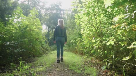following young woman as she walks down bright nature path, lens flare