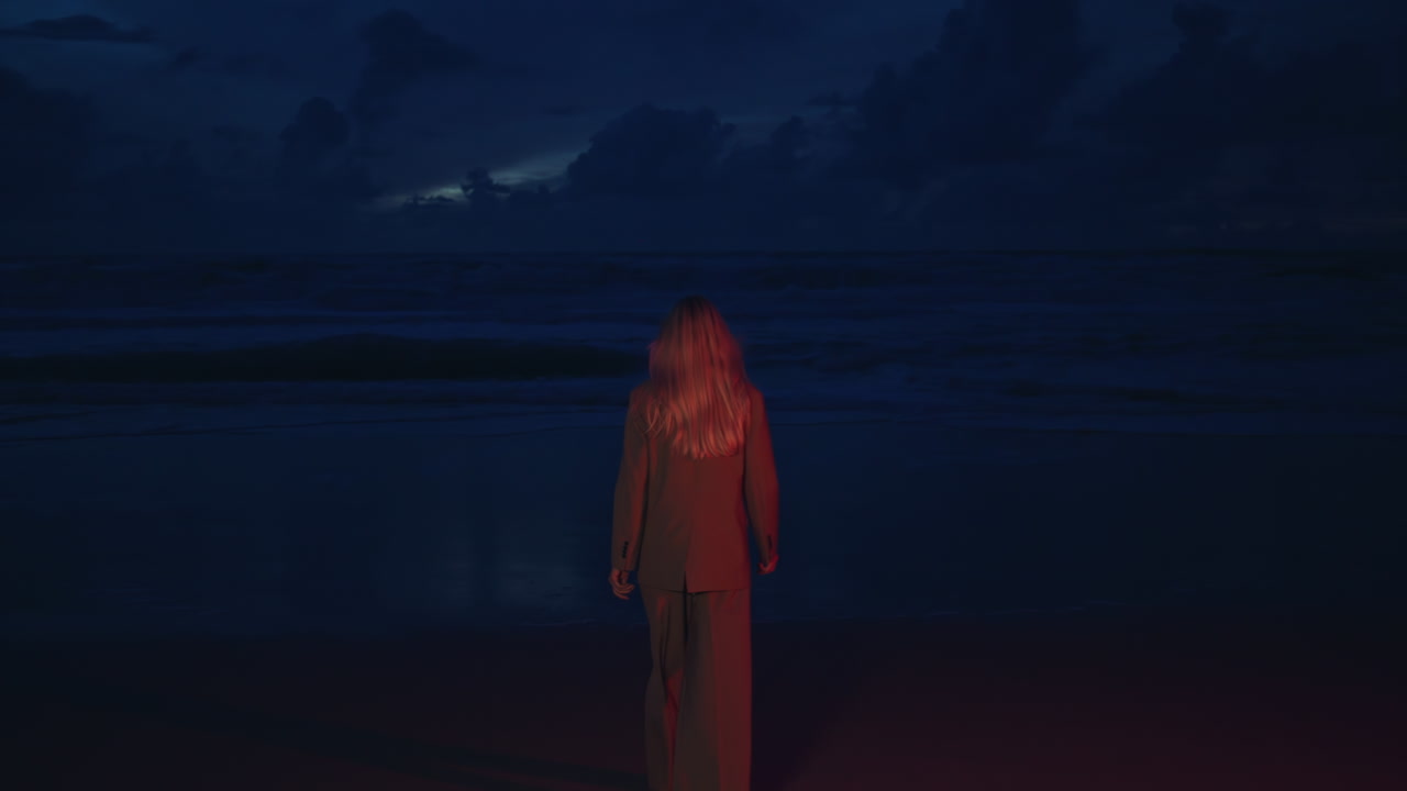 modelo de moda caminando por la noche en la orilla del océano. sexy chica de moda mirando la cámara girar