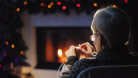 Evening-By-The-Fireplace-On-Christmas-Eve-An-Elderly-Woman-Knits-Warm-Clothes-4k-Video