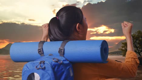 close up back view of a female hiker with mountaineering backpack screaming goal celebrating the success while standing at a lake during sunset time