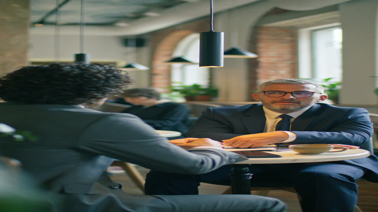 Senior Businessman Speaking with Colleague at Coffee Meeting in Cafe