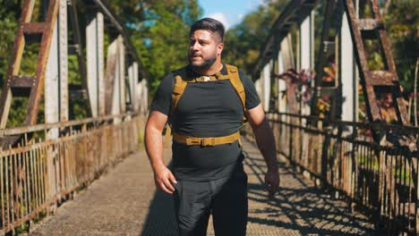 vista frontal joven viajero con mochila caminando por el viejo puente oxidado al aire libre en un soleado día de verano