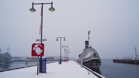 moored boat with covered forward bow tied to snow covered pier dock at aker brygge in winter