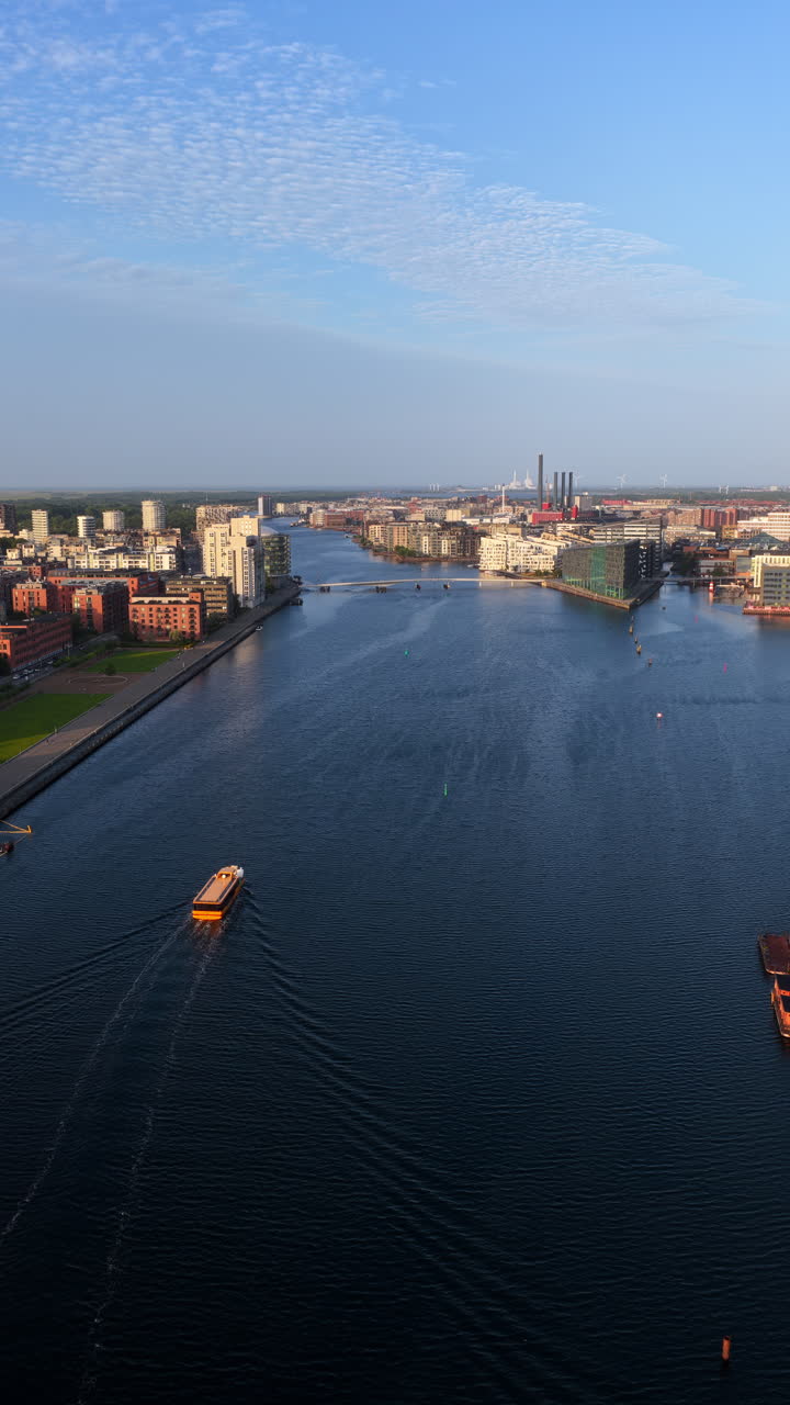 Aerial drone view of the Nyhavn canal and cityscape during golden hour, with boats and modern buildings along the waterfront in Copenhagen, Denmark. Vertical