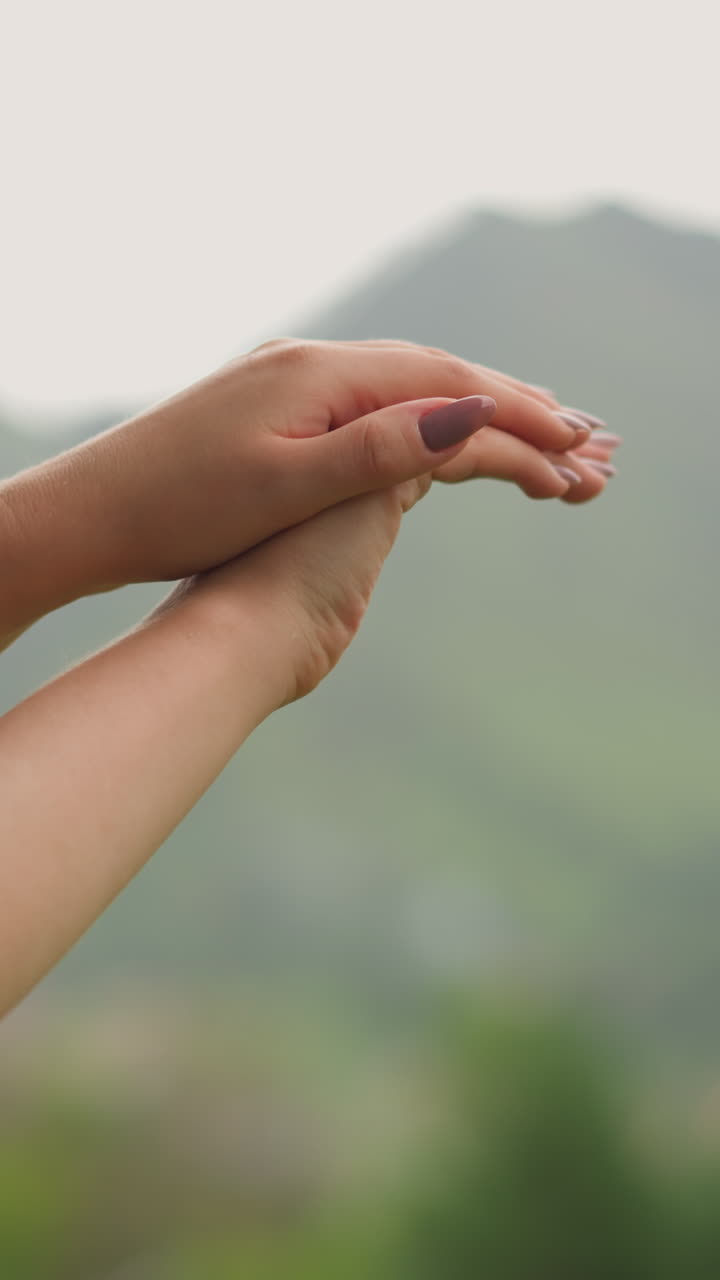 mujer elegante masajes e hidratación manos con estilosa manicura bajo cálidas gotas de lluvia contra las montañas silueta en un día desagradable primer plano cámara lenta
