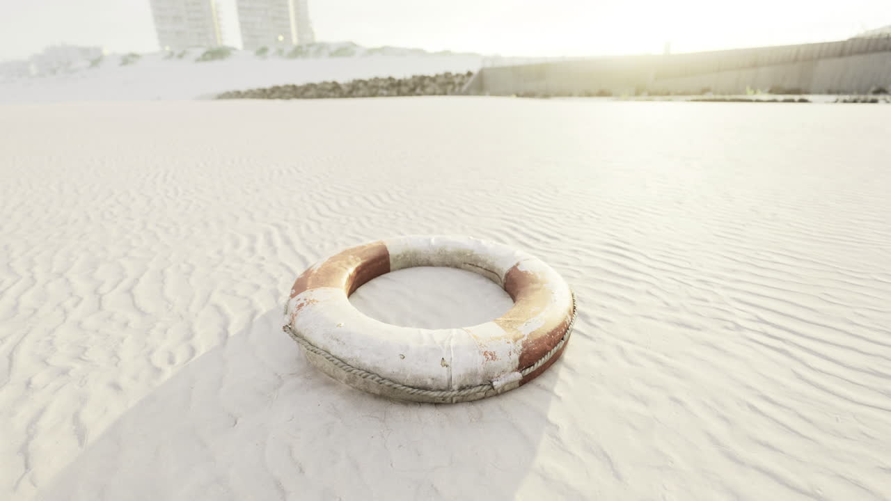 Lifebuoy rests on sandy beach at sunrise near coastal buildings