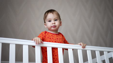 sweet calm caucasian baby standing calmly in the white bed. adorable kid looks up with interest and then laughs cheerfully.
