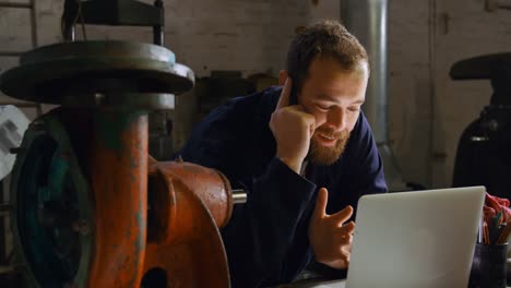 metallschmied spricht am handy in der werkstatt 4k