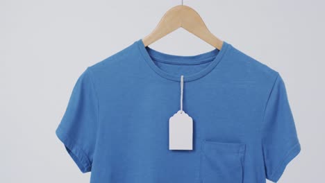 video of blue t shirt with tag on hanger and copy space on white background