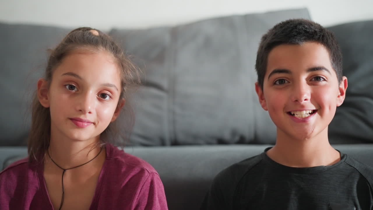 Vista de retrato de un grupo de amigos en el interior mirando directamente a la cámara, con un chico sonriendo alegremente y parpadeando, mientras que la chica mira con calma, creando un ambiente cálido y relajado con una iluminación suave.