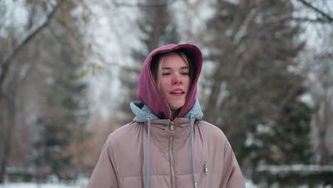 dama corriendo en el parque de invierno frío con expresión facial reflexiva, vestida con una capucha y abrigo cálido, árboles cubiertos de nieve en el fondo