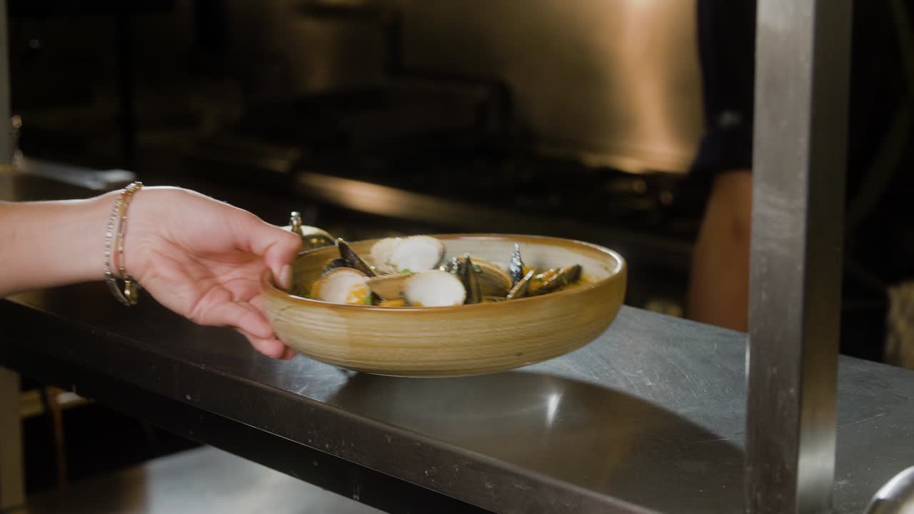 Lo chef consegna un piatto di frutti di mare a un cameriere.