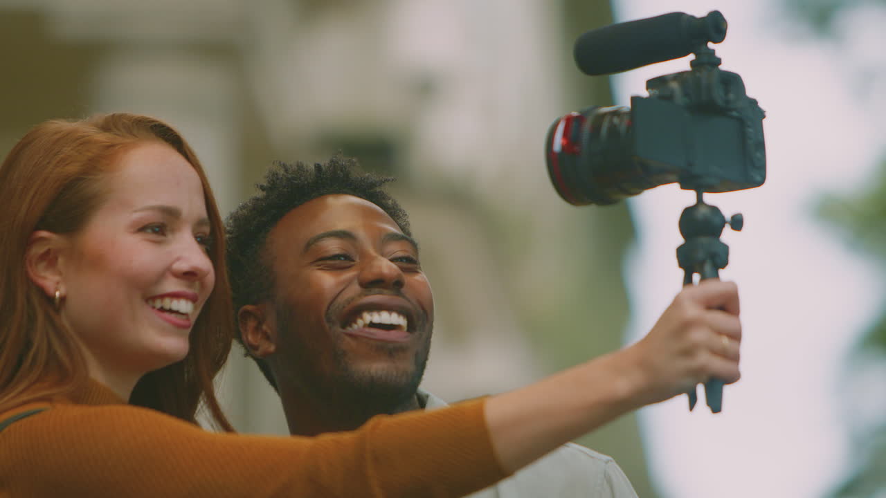 Young Couple Travelling Through City Together Vlogging To Video Camera On Tripod