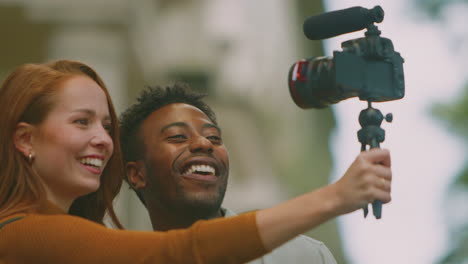 Young-Couple-Travelling-Through-City-Together-Vlogging-To-Video-Camera-On-Tripod