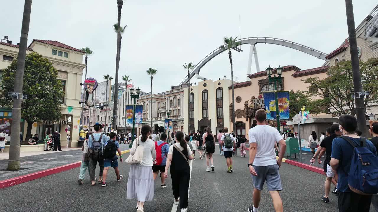 People walking through an amusement park with a roller coaster in the background