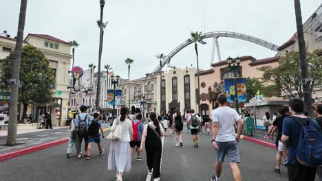 people walking through an amusement park with a roller coaster in the background