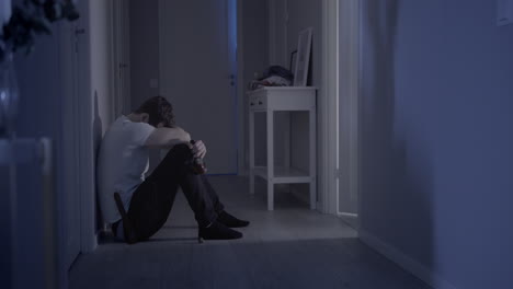 man sitting on the floor of his home depressed, squatting with a bottle of super alcohol in his hand