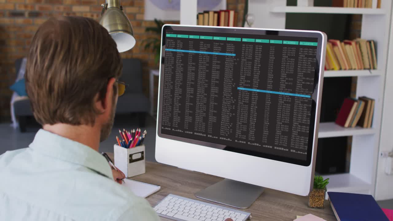 Caucasian man sitting at desk watching coding data processing on computer screen