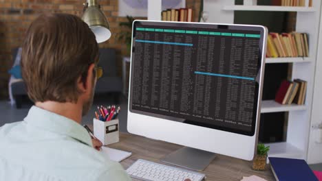 Caucasian-man-sitting-at-desk-watching-coding-data-processing-on-computer-screen