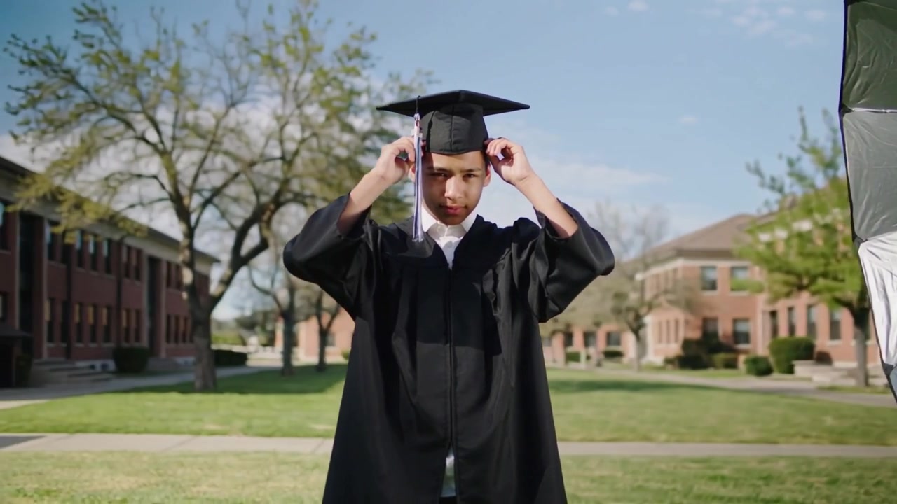 Adjusting grad securing cap while preparing for portrait on campus quad, with black gown and light